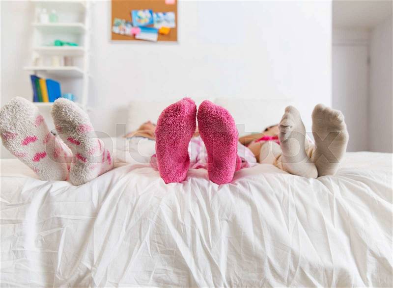Friendship, people and pajama party concept - close up of women feet in socks on bed at home, stock photo