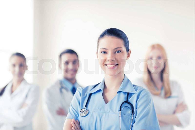 Attractive female doctor or nurse in front of medical group, stock photo