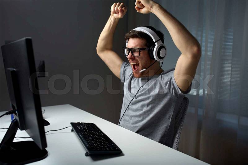 Technology, gaming, entertainment, let\'s play and people concept - happy young man in eyeglasses with headset playing and winning computer game at home and streaming playthrough or walkthrough video, stock photo