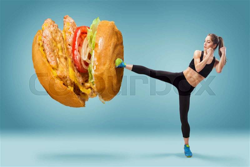 Fit, young, energetic woman boxing unhealthy food on blue background. Concept of diet and healthy lifestile, stock photo