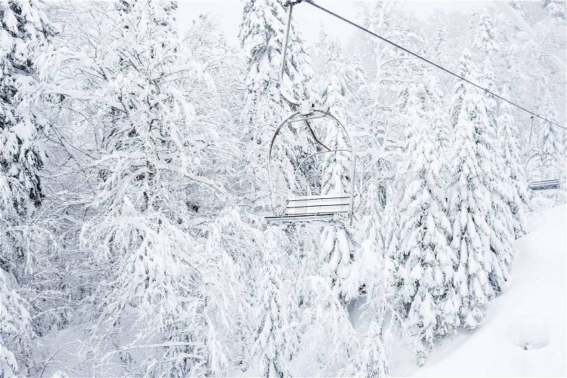 Old cable ski lift with no passengers going across the coniferous forest in 'Kolasin 1450' mountain ski resort near the town of Kolasin in Montenegro after a heavy snowfall on a winter day, stock photo