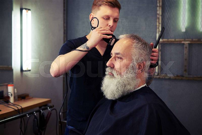 Hairstylist making men\'s haircut to an attractive bearded male in the beauty salon, stock photo