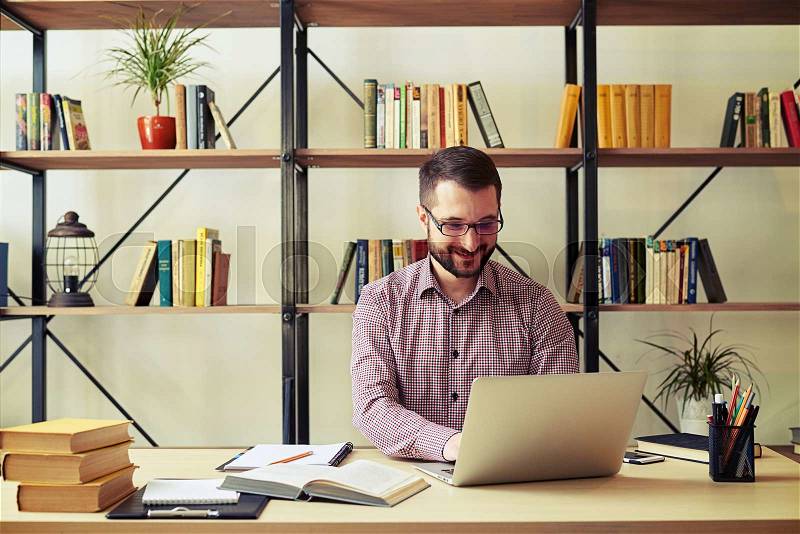 Happy young businessman with the glasses typing on his laptop at home office, stock photo