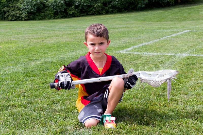 Little boy lacrosse player in the park kneeling down and posing for camera, stock photo