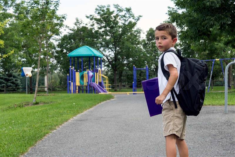 Child with school backpack and book walking in the park, stock photo
