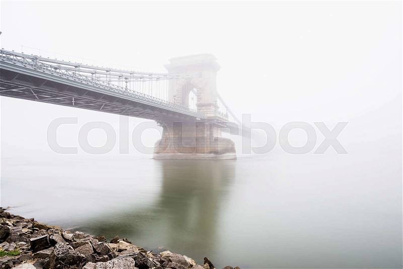 Chain Bridge over the Danube and a boat in Budapest, Hungary, in evening lights, on a foggy day. Shot from the Pest side of the Danube river, stock photo