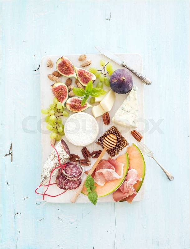Wine and snack set. Figs, grapes, nuts, cheese variety, meat appetizers and herbs on light blue background, top view, stock photo