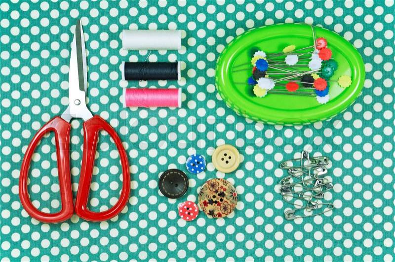 Sawing kit with red scissors and thread on polka dot fabric background, stock photo