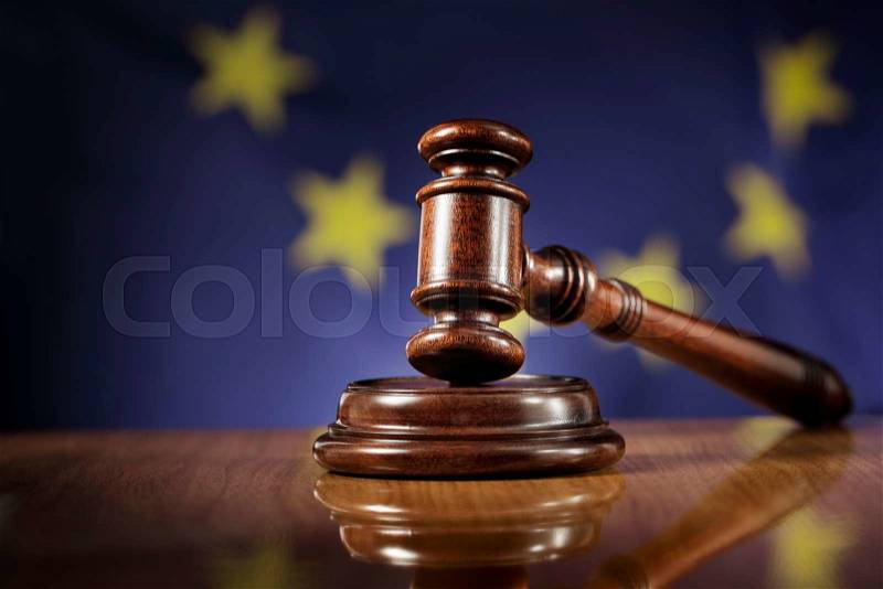 Mahogany wooden gavel on glossy wooden table. Flag of European Union, EU, in the background, stock photo