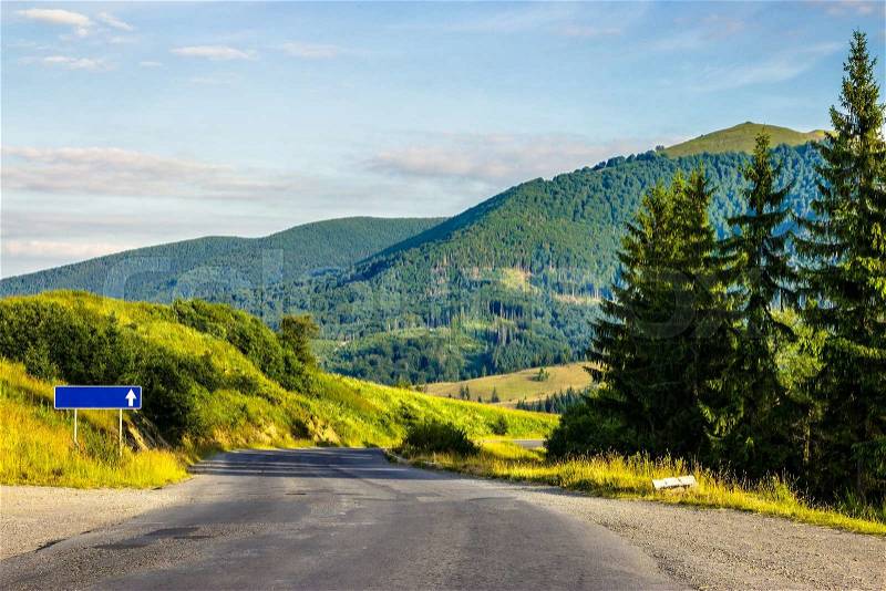 Empty asphalt mountain road near the coniferous forest with cloudy sky in morning light, stock photo
