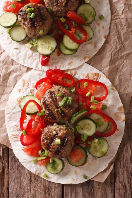 Grilled meat balls with fresh vegetables on a flat bread close up on the table. Vertical view from above\, stock photo