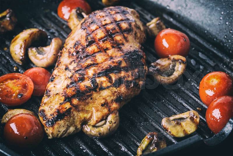 Grilled chicken breast in different variations with cherry tomatoes, mushrooms, herbs, cut lemon on a wooden board or teflon pan. Traditional cuisine. Grill kitchen, stock photo