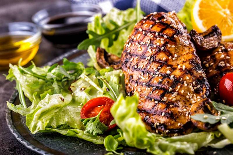 Grilled chicken breast in different variations with lettuce salad cherry tomatoes mushrooms herbs cut lemon on a wooden board or teflon pan. Traditional cuisine. Grill kitchen, stock photo