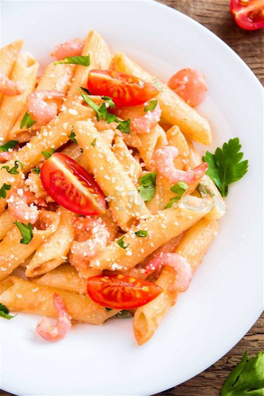 Penne pasta with shrimps, tomato sauce, parsley and grated parmesan cheese over rustic wooden background, stock photo