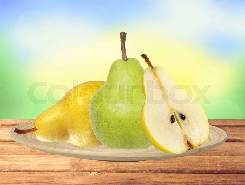 Beautiful fresh green and yellow pears on plate on table over nature, stock photo