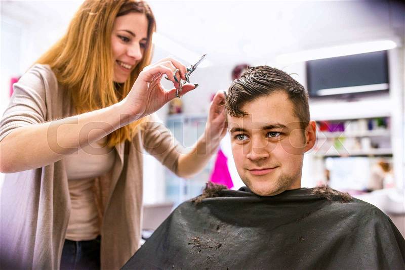 Professional hairdresser cutting hair of her young client, making a new haircut. Barber at work. Man at barbershop, stock photo