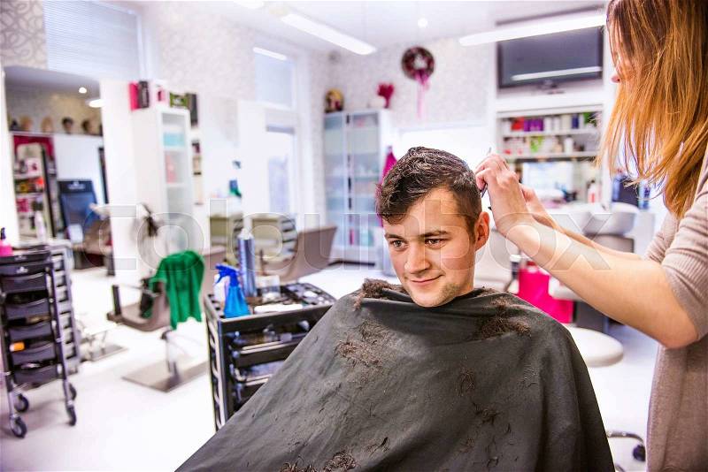Unrecognizable professional hairdresser cutting hair of her young client, making a new haircut. Barber at work. Man at barbershop, stock photo