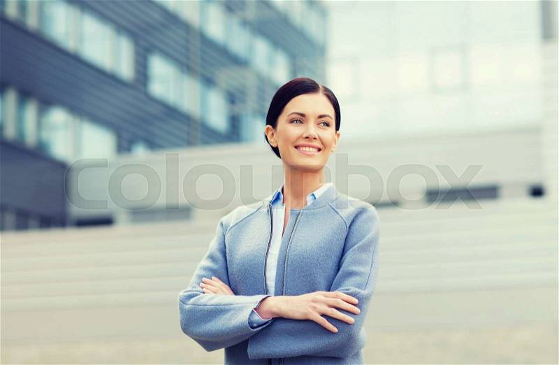 Business and people concept - young smiling businesswoman over office building, stock photo