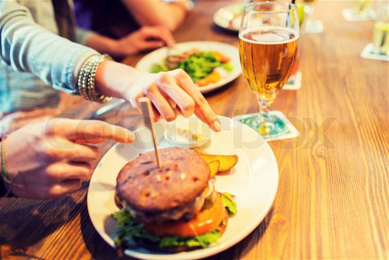 People, leisure, friendship, eating and food concept - close up of friends hands with burger at bar or pub, stock photo