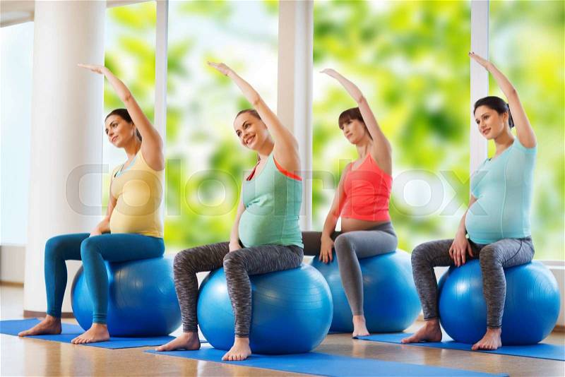 Pregnancy, sport, fitness, people and healthy lifestyle concept - group of happy pregnant women exercising on ball in gym, stock photo