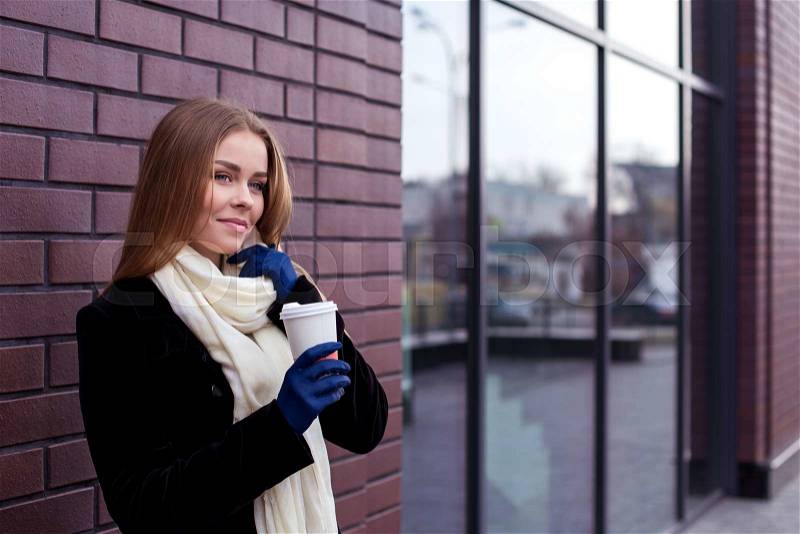 Young stylish woman drinking coffee to go in a city street, stock photo