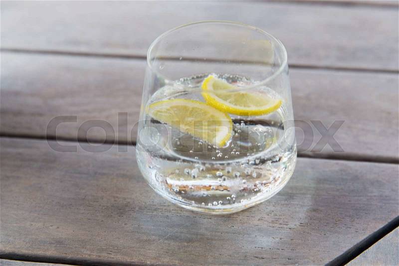 Drink and refreshment concept - glass of sparkling water with lemon slices on table, stock photo