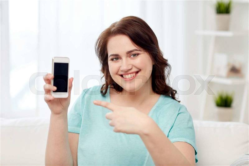 People, technology, communication and leisure concept - happy young plus size woman sitting on sofa and showing smartphone blank screen at home, stock photo