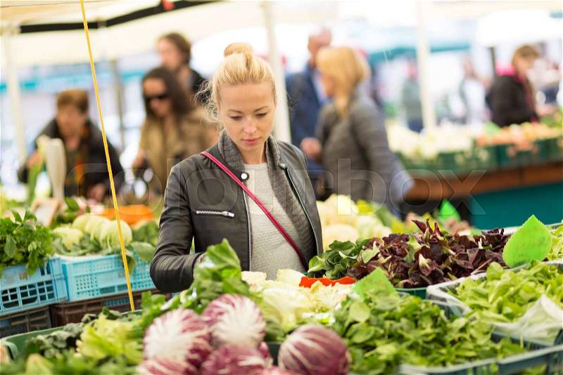 Woman buying fruits and vegetables at local food market. Market stall with variety of organic vegetable, stock photo