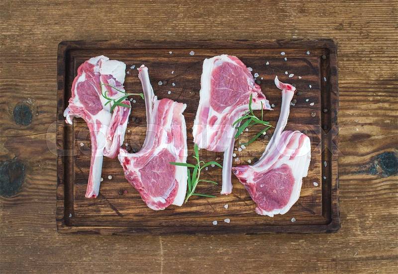 Raw lamb chops. Rack of Lamb with rosemary and spices on rustic chopping board over old wooden background, top view, stock photo