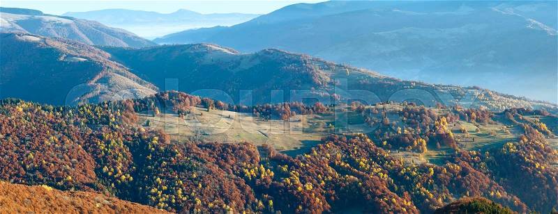 Sunbeam and autumn misty morning mountain panorama with colorful trees on slope, stock photo