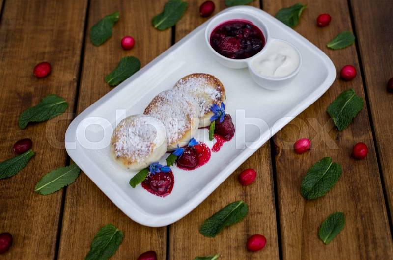 Cheese cakes with berry jam and sour cream. on a wooden background, stock photo