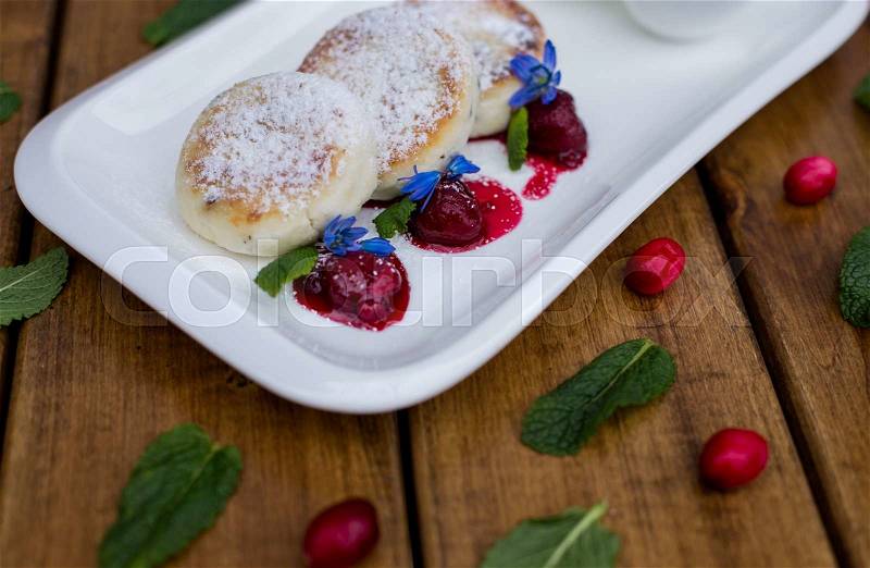 Cheese cakes with berry jam and sour cream. on a wooden background, stock photo
