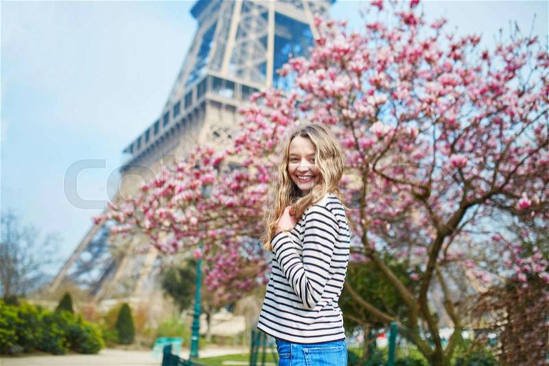 Cheerful young girl in Paris near the Eiffel tower and pink magnolia in full bloom, stock photo