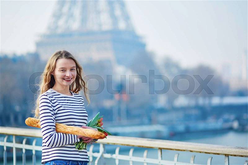 Beautiful young girl with fresh tasty traditional French bread (baguette) and tulips near the Eiffel tower, stock photo