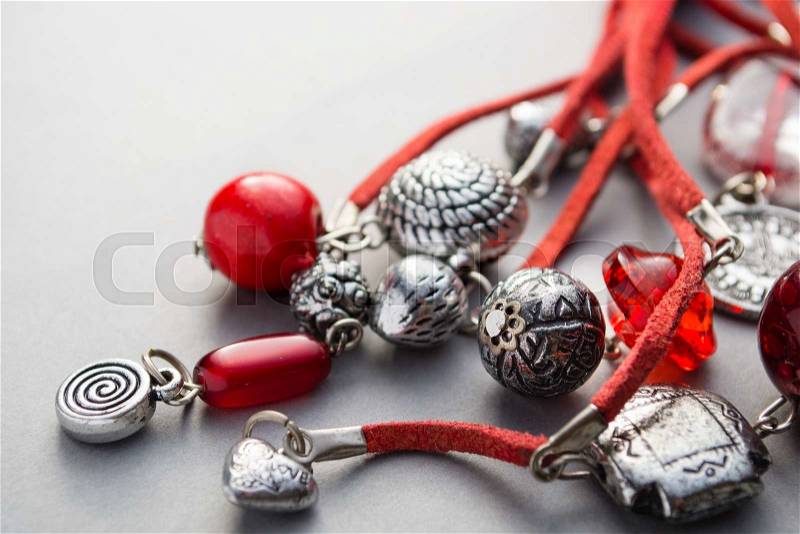 Close up of red glass beads and silver charms attached to leather string on gray background, stock photo