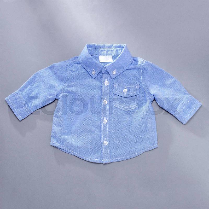 Little blue infant buttoned long sleeve shirt with front pocket on gray background, stock photo