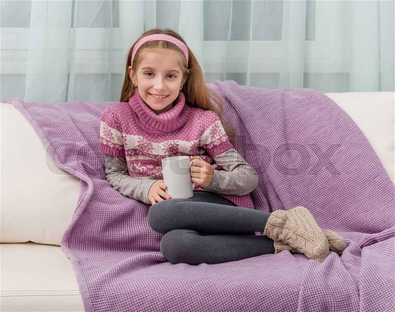 Lovely little girl on a sofa with warm blanket holding a cup of tea, stock photo