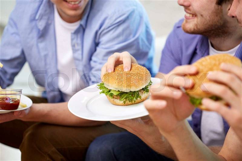 Fast food, unhealthy eating, people and junk-food - close up of happy friends eating hamburgers at home, stock photo