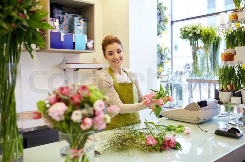 People, business, sale and floristry concept - happy smiling florist woman making tulip bunch at flower shop, stock photo