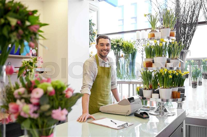 People, sale, retail, business and floristry concept - happy smiling florist man with clipboard and cashbox standing at flower shop counter, stock photo