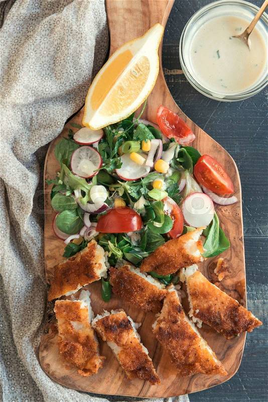 Served sliced catfish fillets with healthy salad on wooden board , stock photo