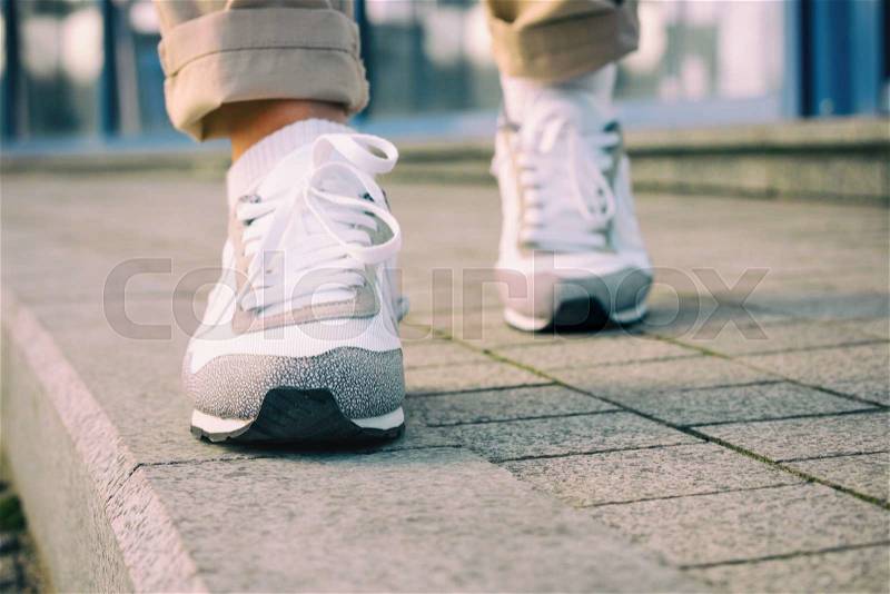 Female feet in white sneakers walking on the sidewalk, low angle, retro colors, stock photo