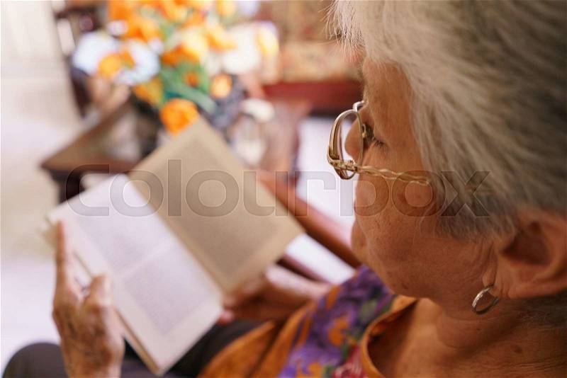 Old people in geriatric hospice: senior woman with eyeglasses and miopia problems sitting on chair and reading a book. , stock photo