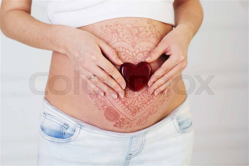 Fashion henna tattoo mehendi on pregnant belly and glass heart, stock photo