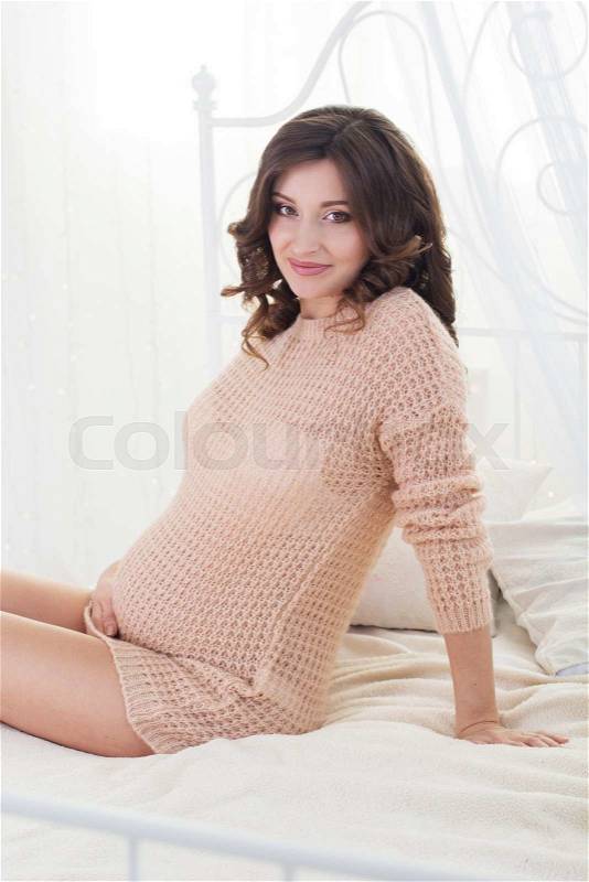 Young pregnant girl is sitting on bed, stock photo