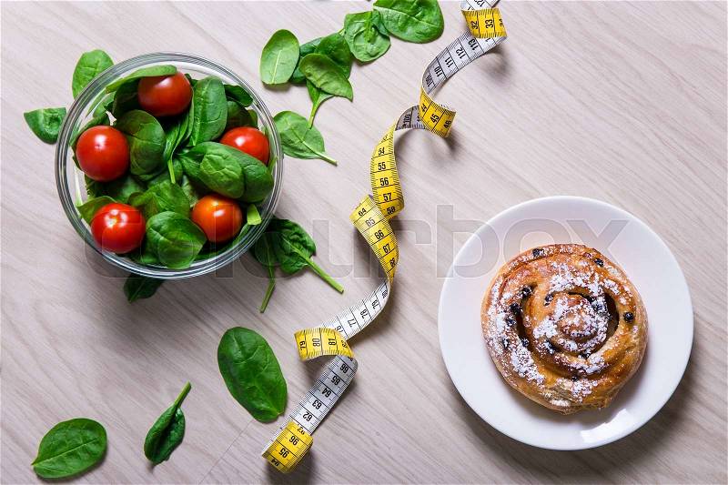 Diet and weight loss concept - healthy salad with spinach and tomatoes, measure tape and sweet bun with raisins, stock photo