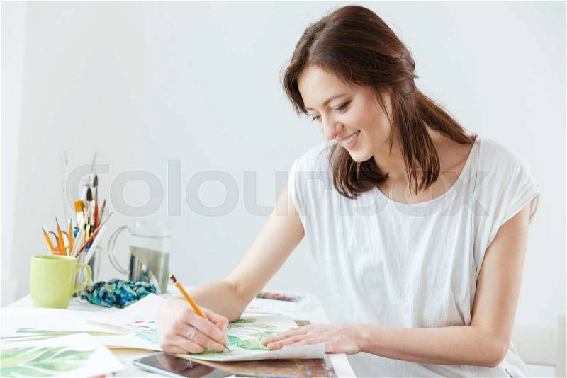 Smiling pretty woman painter drawing at the table , stock photo