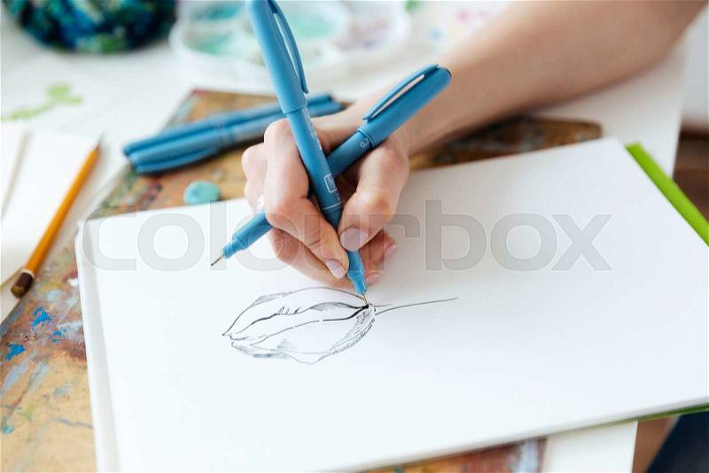 Closeup of hands of woman artist drawing with gel ink pen ayt the table , stock photo