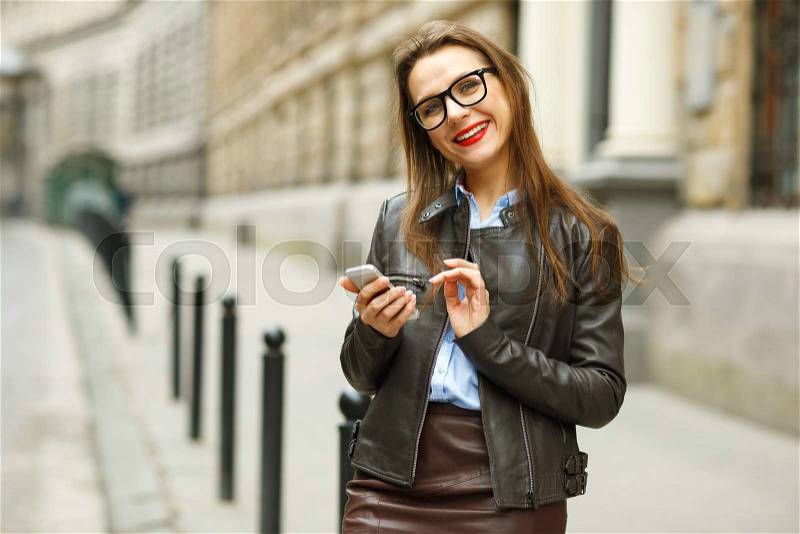 Businesswoman walking down the street while using the smart phone. Happy smiling caucasian business woman busy, stock photo