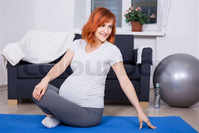 Young pregnant woman doing fitness exercises at home, stock photo